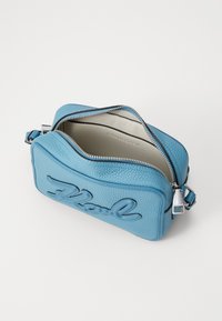 Geantă crossbody din piele texturată albastră, cu închidere cu fermoar, având un detaliu logo reliefat pe față și un interior în contrast.
