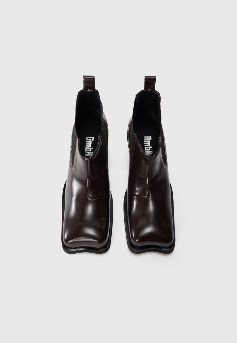 Bottes de chevilles marron brillantes au design épuré, avec des panneaux latéraux élastiques et une forme de pointe carrée sur une semelle en caoutchouc noir.