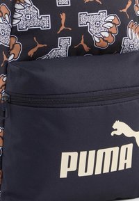 Mochila negra con un diseño estampado que presenta logotipos de PUMA en tonos de marrón y blanco. Incluye un bolsillo frontal con cremallera y tejido texturizado.