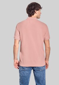 Rosa polo skjorta, korta ärmar, ribbad krage, enkel design, mjukt material. Bärs med blå denimjeans, visande bakvy.