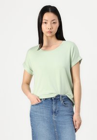 Hellgrünes T-Shirt mit kurzen Ärmeln und umgeschlagenen Bündchen, runder Ausschnitt und weicher Textur, kombiniert mit einem Jeansrock.