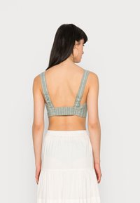 Bralette verde com riscas, com alças largas, tecido texturizado e um design de costas baixas. Combinado com uma saia branca em camadas, exibido de costas.