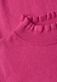 Gros plan d'un pull tricoté rose vif plié montrant un col rond côtelé et une texture de tissu douce.
