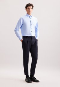 Lichtblauw overhemd met lange mouwen en een knoopsluiting, met een enkele borstzak, gecombineerd met op maat gemaakte zwarte broeken en zwarte schoenen.