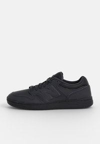 Baskets de sport noires en matériau synthétique, design bas, fermeture à lacets et logo accentué sur le côté. Semelle texturée pour une meilleure adhérence.