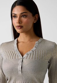 Hellgrauer Strickcardigan mit vertikaler Rippung, Knopfleiste am Ausschnitt und dezenten Strukturvariationen. Weicher Stoff mit mittlerer Dehnbarkeit.