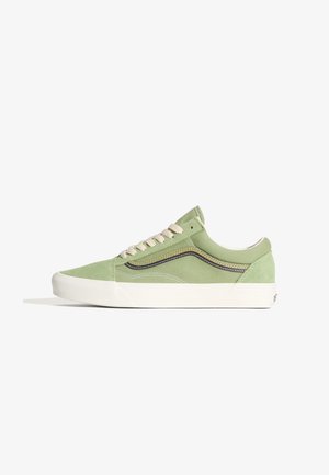 Sneakers in tela verde con lacci crema, suola in gomma bianca, design classico con striscia laterale in cuciture marroni e gialle. Profilo low-top.