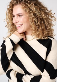 Grofgebreide trui met strepen in crème en zwart, met brede horizontale strepen, een geribbelde textuur en een hoge hals.