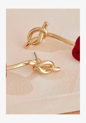 Orecchini in tono dorato con un design annodato e finitura lucida, accentuati da dettagli rossi e fissati con chiusura a perno.