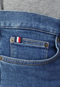 Jeans aus Denim in einem blauen Farbton, mit einem kleinen rot-weiß-blauen Etikett in der Vorderseite der Tasche, sichtbaren Nähten und Knopf-Beschlägen.
