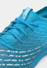 Ανοιχτό μπλε αθλητικό παπούτσι με υφή στην επιφάνεια, με λευκά γεωμετρικά σχέδια, επίπεδα κορδόνια και ετικέτα που γράφει "MAGNETICO".