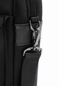 Czarny pasek z tkaniny i skóry połączony z metalowym obrotowym karabińczykiem na rogu czarnej, teksturowanej torby.