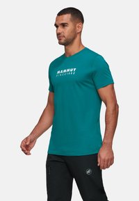 Aqua kleurige t-shirt met korte mouwen van katoen en een ronde halslijn. Voorzien van een witte grafische opdruk met de tekst "MAMMUT SINCE 1862" aan de voorkant.
