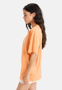 Orange Baumwoll-T-Shirt mit kurzen Ärmeln, mit einem lockeren Schnitt und grafischem Design auf der Vorderseite. Glatte Textur und klassischer Rundhalsausschnitt.