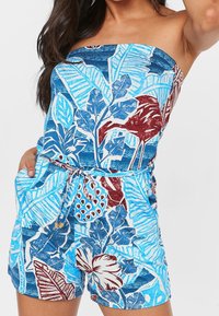 Robe courte à imprimé floral bleu avec un design sans bretelles, taille cintrée et poches, présentant des textures et des motifs de feuilles et de fleurs.