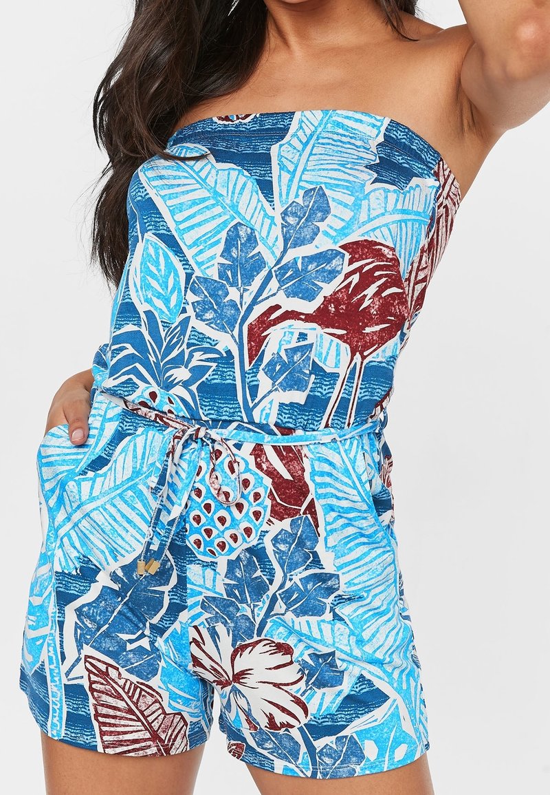 Robe courte à imprimé floral bleu avec un design sans bretelles, taille cintrée et poches, présentant des textures et des motifs de feuilles et de fleurs.