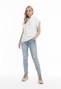 Fehér, rövid ujjú kapucnis pulóver, kapucnival és zsinórral, világoskék, szakadt skinny farmernadrággal és világosbarna fűzős bokacsizmával párosítva.