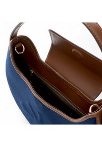 Marineblaue Canvas-Tasche mit braunen Lederelementen, ausgestattet mit einer Reißverschlusstasche und einem Klappverschluss. Innen hat sie eine glatte Textur.