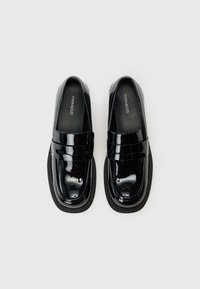 Mocassins en cuir verni noir avec une semelle en caoutchouc plate, un bout arrondi et une bande décorative à l'avant avec des détails de couture.