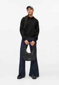 Black hoodie, wide-leg denim pants with side slits, and a black nylon hobo bag. Model wears a gray cap and black boots.