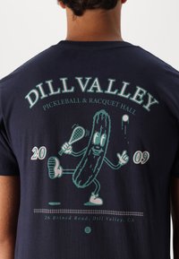 Dunkelblaues Baumwoll-T-Shirt mit einem Grafikmotiv eines Cartoon-Gurkens, der einen Schläger hält, mit dem Text "DILL VALLEY PICKLEBALL & RACQUET HALL" und dem Datum.
