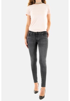 Camiseta rosa claro, ajustada al cuerpo, de manga corta. Pantalones vaqueros ajustados gris oscuro con cinco bolsillos y adornos. Tacones altos negros completan el look.