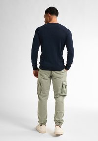 Mörkblå långärmad tröja kombinerad med ljusgröna cargobyxor med sidofickor och elastiska muddar, bärs med beigefärgade sneakers.