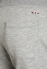 Pantaloni della tuta grigi caratterizzati da un tessuto testurizzato, una vita a coste e un dettaglio ricamato con accenti rossi, bianchi e blu vicino alla tasca.