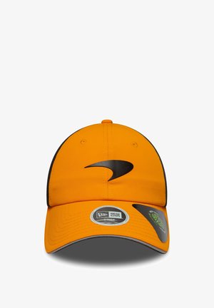 Pomarańczowa czapka z materiału z czarnym logo z przodu. Posiada zakrzywiony daszek i markowe metki na spodniej stronie.