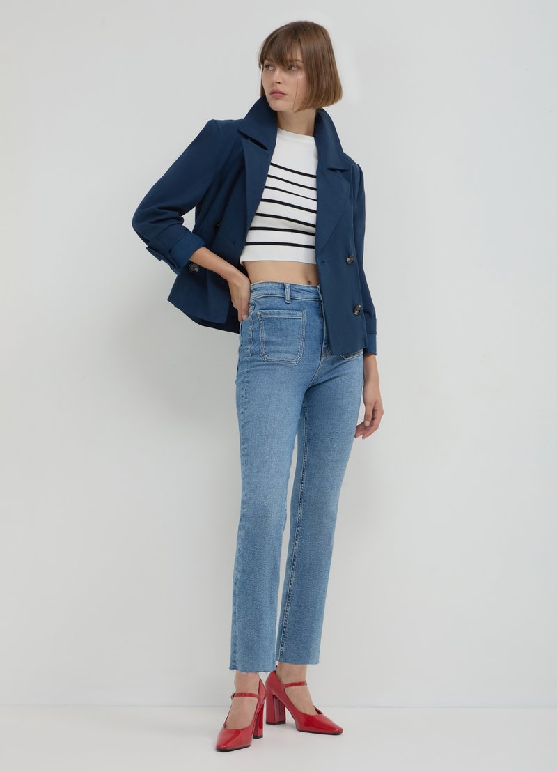 Marineblaue zweireihige Jacke, weiß gestreiftes bauchfreies Top, hellblaue hoch taillierte Jeans, rote Absätze, glatte Textur und figurbetontes Design.