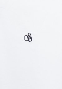 Witte polo gemaakt van textuurstof, met een klein zwart "&"-logo geborduurd aan de linkerkant. Eenvoudig ontwerp, geen patronen of accenten.