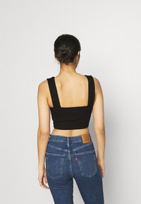 Top negro corto con tirantes anchos, combinado con jeans de mezclilla azul de cintura alta que presentan un parche de cuero en la parte trasera. Textura suave.