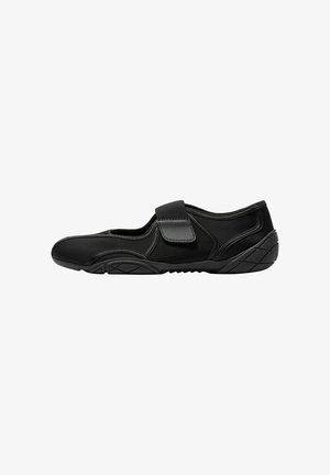 Black shoe with a fabric upper and mesh panels, featuring a hook-and-loop strap. The sole has a textured pattern for grip.