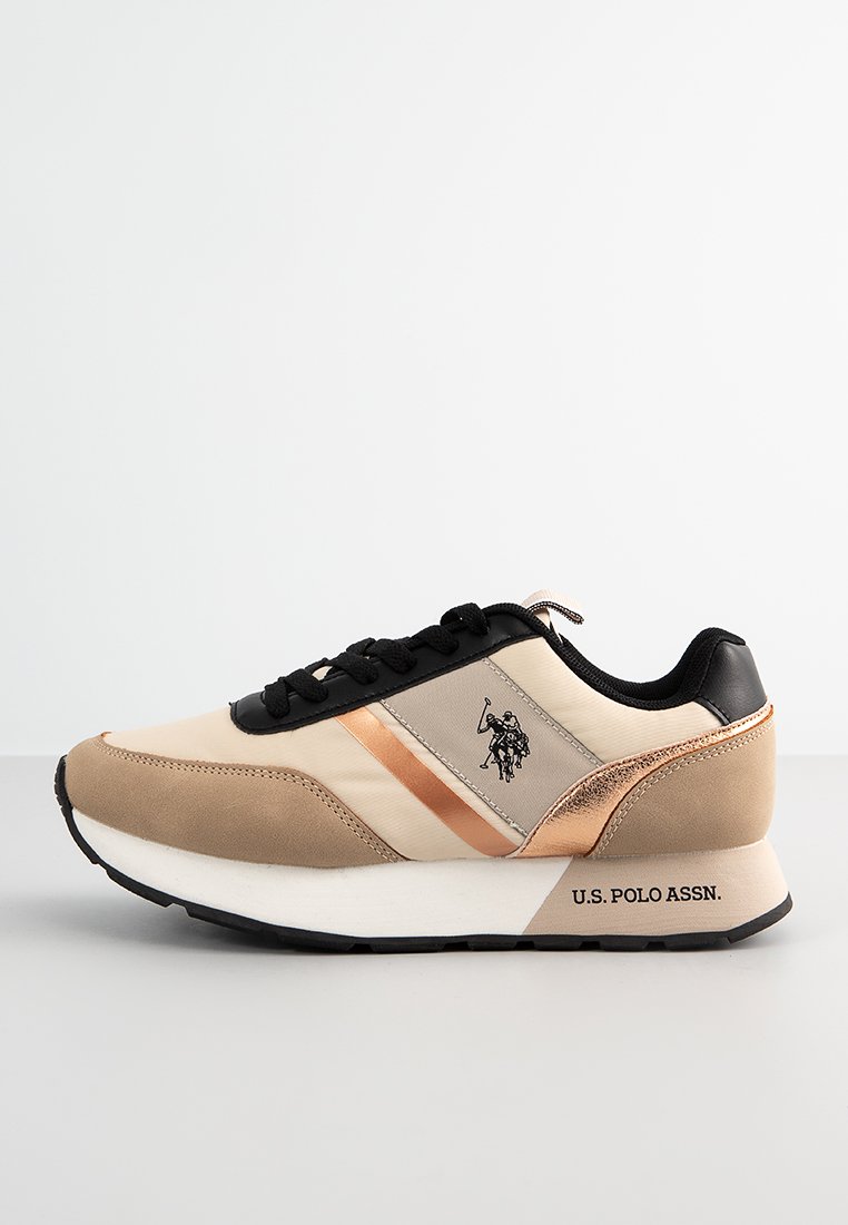 Zapatillas beige y negras con acentos en oro rosa. Presentan una parte superior de textil suave, franjas contrastantes y detalle del logo en el lado y el talón.