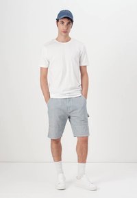 Bílá bavlněná tričko, modré pruhované šortky, bílé tenisky a světle modrá čepice s malým logem. Jednoduchý, neformální outfit v neutrálních barvách.