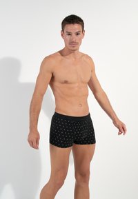 Schwarze Boxer-Brief mit einem gemusterten Design, das kleine Kreise zeigt. Sie bestehen aus weichem Stoff, haben eine enge Passform und einen schwarzen elastischen Bund.