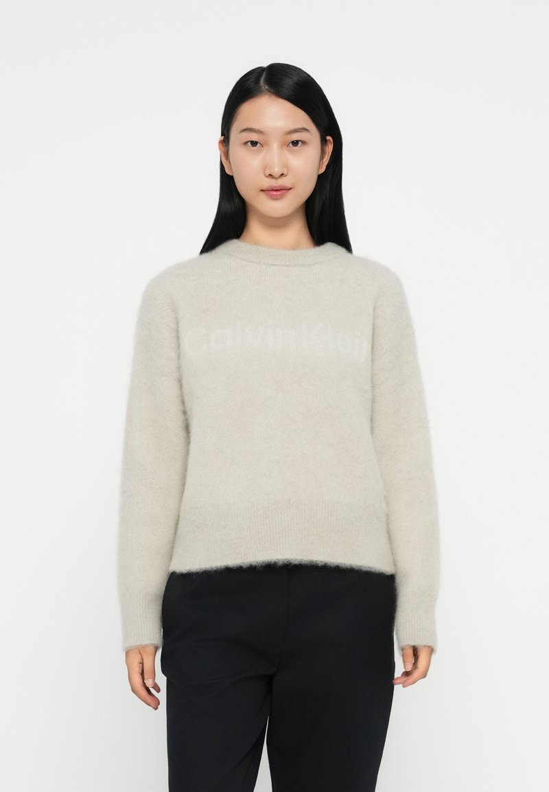 Lichtgrijze trui met een zachte, fluffy textuur, featuring een ronde halslijn en de merknaam "Calvin Klein" subtiel afgebeeld aan de voorkant.