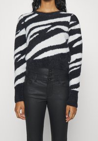 Pull rayé noir et blanc en matière douce et duveteuse, avec un col rond et des poignets côtelés, associé à un pantalon noir en similicuir taille haute.