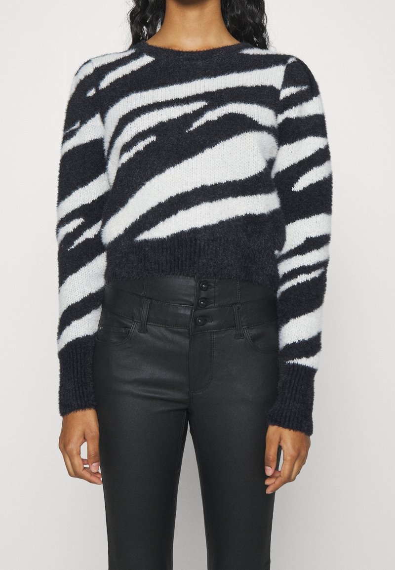 Pull rayé noir et blanc en matière douce et duveteuse, avec un col rond et des poignets côtelés, associé à un pantalon noir en similicuir taille haute.