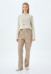 Lichtbeige lange mouwtop met sterren- en maanprint; bruine geblokte broek met hemelse ontwerpen; zachte stof; gestrikt tailleband.