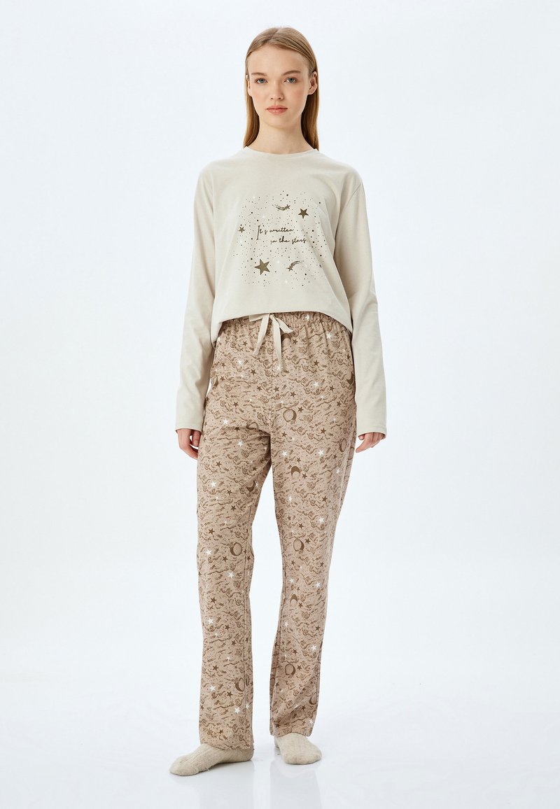 Lichtbeige lange mouwtop met sterren- en maanprint; bruine geblokte broek met hemelse ontwerpen; zachte stof; gestrikt tailleband.