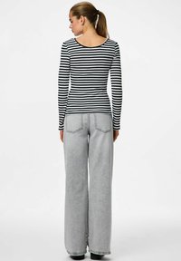 Černobíle pruhovaný top s dlouhými rukávy v kombinaci s šedými, vysokým pasem a širokými džíny. Tento outfit má přiléhavý siluetu a hladkou texturu.