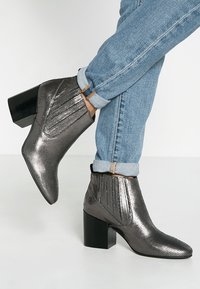 Metallisch graue Knöchelstiefel mit einem eleganten Design, strukturierter Oberfläche und Blockabsatz. Verfügt über elastische seitliche Einsätze für ein einfaches An- und Ausziehen.