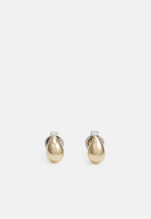 Paire de petites boucles d’oreilles clous en forme de goutte dorée brillante avec dos de couleur argent sur un fond clair uni.