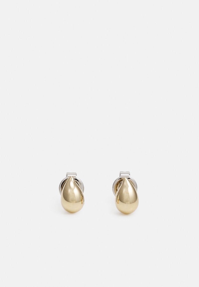 Paire de petites boucles d’oreilles clous en forme de goutte dorée brillante avec dos de couleur argent sur un fond clair uni.