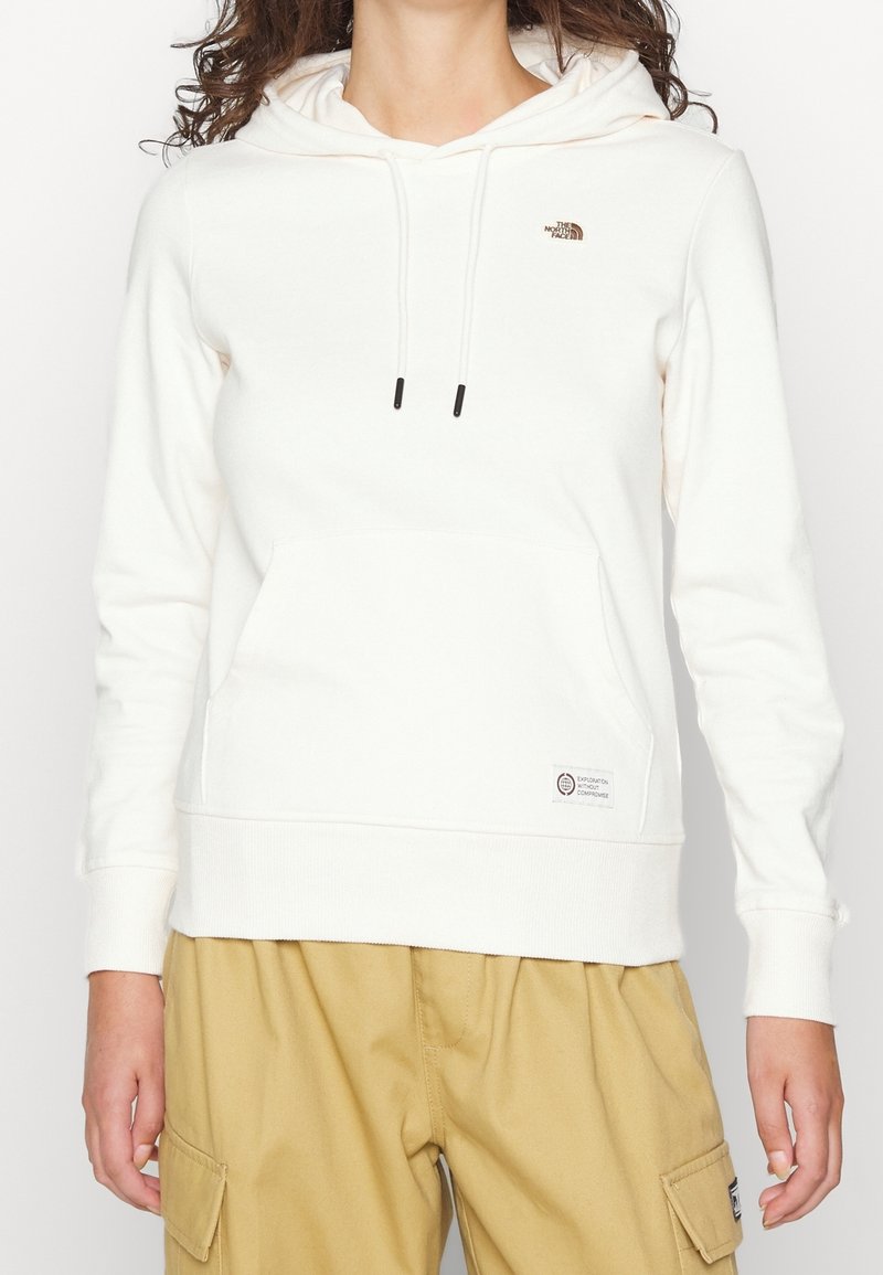 Sudadera blanca con un bolsillo frontal, cordones y un pequeño logo en el pecho. Material de algodón, puños acanalados y una etiqueta cerca del dobladillo.