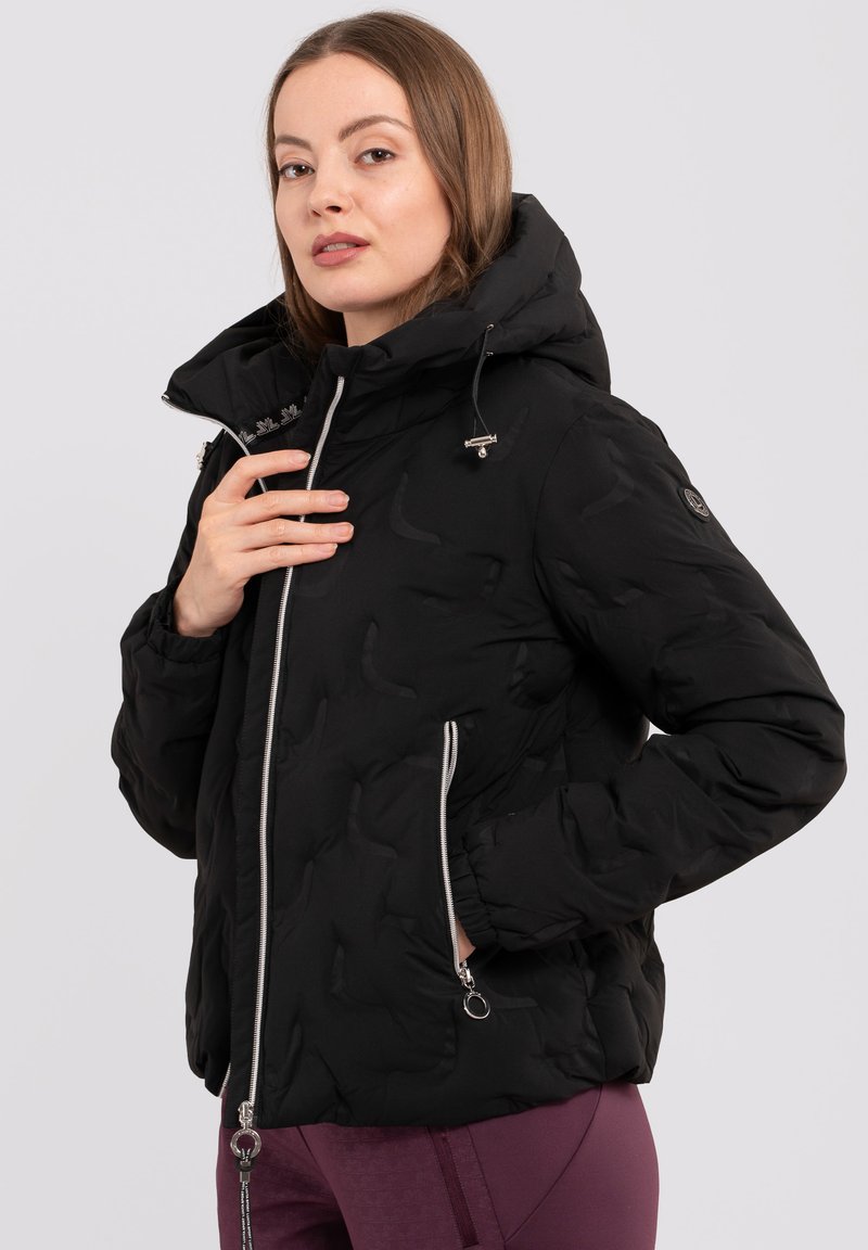 Schwarze Pufferjacke mit Kapuze, ausgestattet mit metallischen Reißverschlüssen, Seitentaschen und einem strukturierten Muster auf dem Stoff. Silberne Hardware-Details.