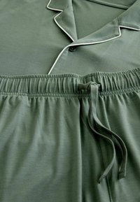 Ensemble de pyjama vert doux avec passepoil blanc sur le col et le haut boutonné, taille élastiquée et cordon de serrage noué sur le pantalon.
