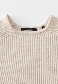Beige Rippstrickpullover mit Rundhalsausschnitt und schwarzem Etikett mit der Aufschrift "irgendwann" im Kragen.