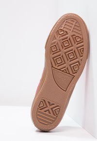 Suela de una zapatilla roja Converse All Star mostrando un detallado patrón de tracción marrón y el logo de la marca contra un fondo blanco.